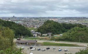 観法寺PA脇の丘陵上から海側を見た写真。中央に今年度の調査区が、左奥遠くに県庁が見えます。