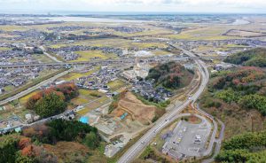 上空から見たところ。遠くに日本海とかほく潟、手前に観法寺ヤッタ遺跡の調査区と観法寺墳墓群。山側環状道路や新幹線線路も見えます。