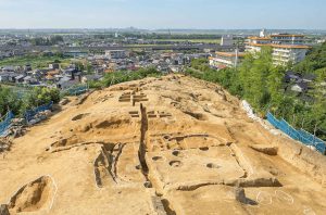 丘陵上の観法寺墳墓群を東の山側から見ています。竪穴建物と墳丘墓が調査されており、はるか彼方には河北潟が見えます。