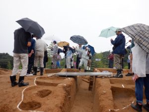 現地説明会で観法寺墳墓群1号墓の説明をしているところです。小雨の中、多くの見学者が説明に聞き入っています。